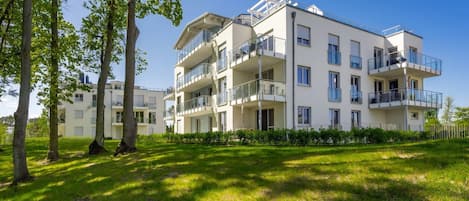 A multi-story residential building with balconies, surrounded by greenery and trees.