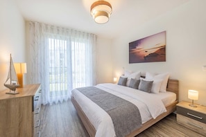 A hotel room with a bed, bedside tables, a lamp, a sailboat decoration, and a painting of a sunset. - Ferienwohnung Klippenblick (Garz)