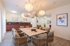 A modern dining area with a wooden table and wicker chairs, a kitchen in the background, and pendant lighting. - Ferienwohnung Klippenblick (Garz)