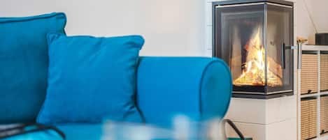 Een moderne woonkamer met een blauwe bank, een gashaard met glazen front en een witte muur.