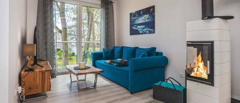 A modern living room with a blue sofa, a small wooden table, a fireplace, and a window with curtains.