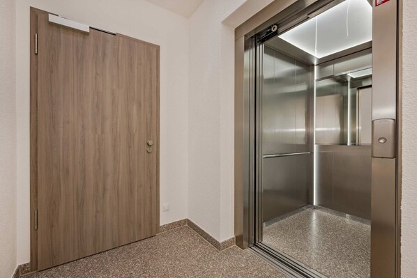 A hallway with a wooden door and a modern elevator.