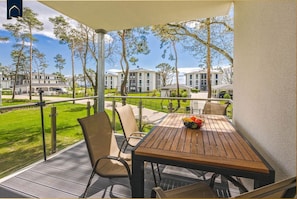 A covered outdoor seating area with a table and chairs, a fruit bowl, and a view of buildings in the background.