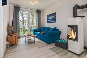 A living room with a blue sofa, a wooden coffee table, a fireplace, and a window with curtains. - Ferienwohnung Meerzeit - Hochwertiges Appartement in Ruhiger Lage, mit Terrasse, Kostenfreier Sauna (Zirchow)