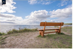 A wooden bench by a body of water with a clear sky. - Ferienwohnung Meerzeit - Hochwertiges Appartement in Ruhiger Lage, mit Terrasse, Kostenfreier Sauna (Zirchow)