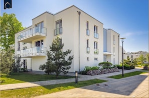 A modern multi-story residential building with balconies, a well-maintained lawn, and a clear sky. - Ferienwohnung Meerzeit - Hochwertiges Appartement in Ruhiger Lage, mit Terrasse, Kostenfreier Sauna (Zirchow)