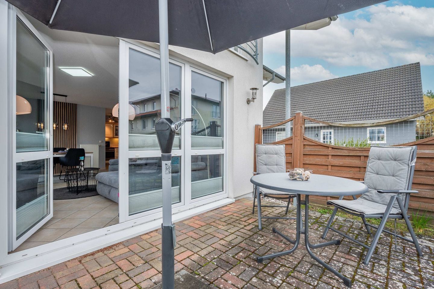 Eine Terrasse mit Tisch und Stühlen, eine Schiebetür zu einem Innenbereich und ein Holzzaun im Hintergrund.