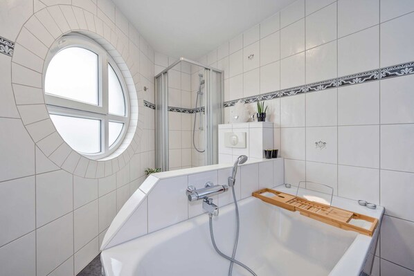 A modern bathroom with a bathtub, shower, and a round window.