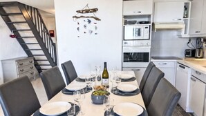 Comedor con una mesa dispuesta para cuatro, una cocina al fondo y una escalera que lleva a otro nivel.