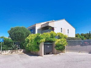 Un bâtiment moderne doté d’un balcon, d’un panneau indiquant un espace de stationnement et d’une entrée fermée par un portail.