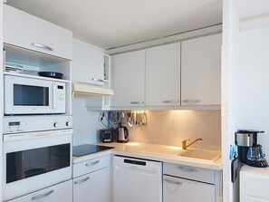 Una cocina moderna con armarios blancos, microondas integrado, lavavajillas y cafetera.