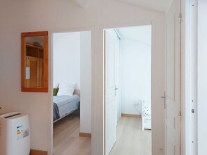 Un couloir étroit mène à une chambre qui contient un lit, une petite table et une armoire blanche.