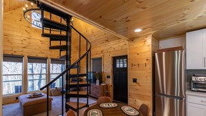 Interior d'una cabana amb una escala espiraltraçada, parets de fusta, zona de dinar amb taules rodones i cuina amb electrodomèstics d'acer inoxidable.