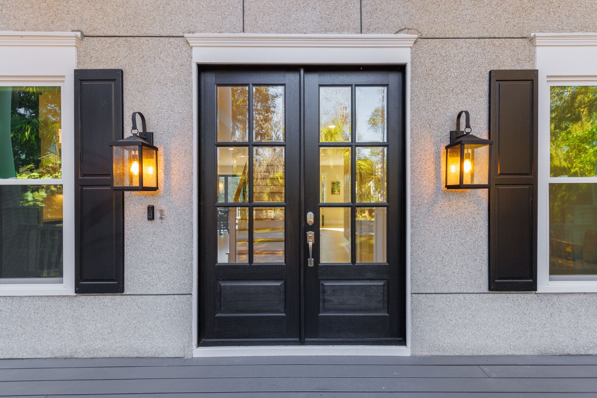 A black double door with a glass panel, flanked by two black lantern-style lights and a textured stone wall.