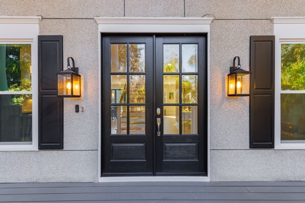 A black double door with a glass panel, flanked by two black lantern-style lights and a textured stone wall.