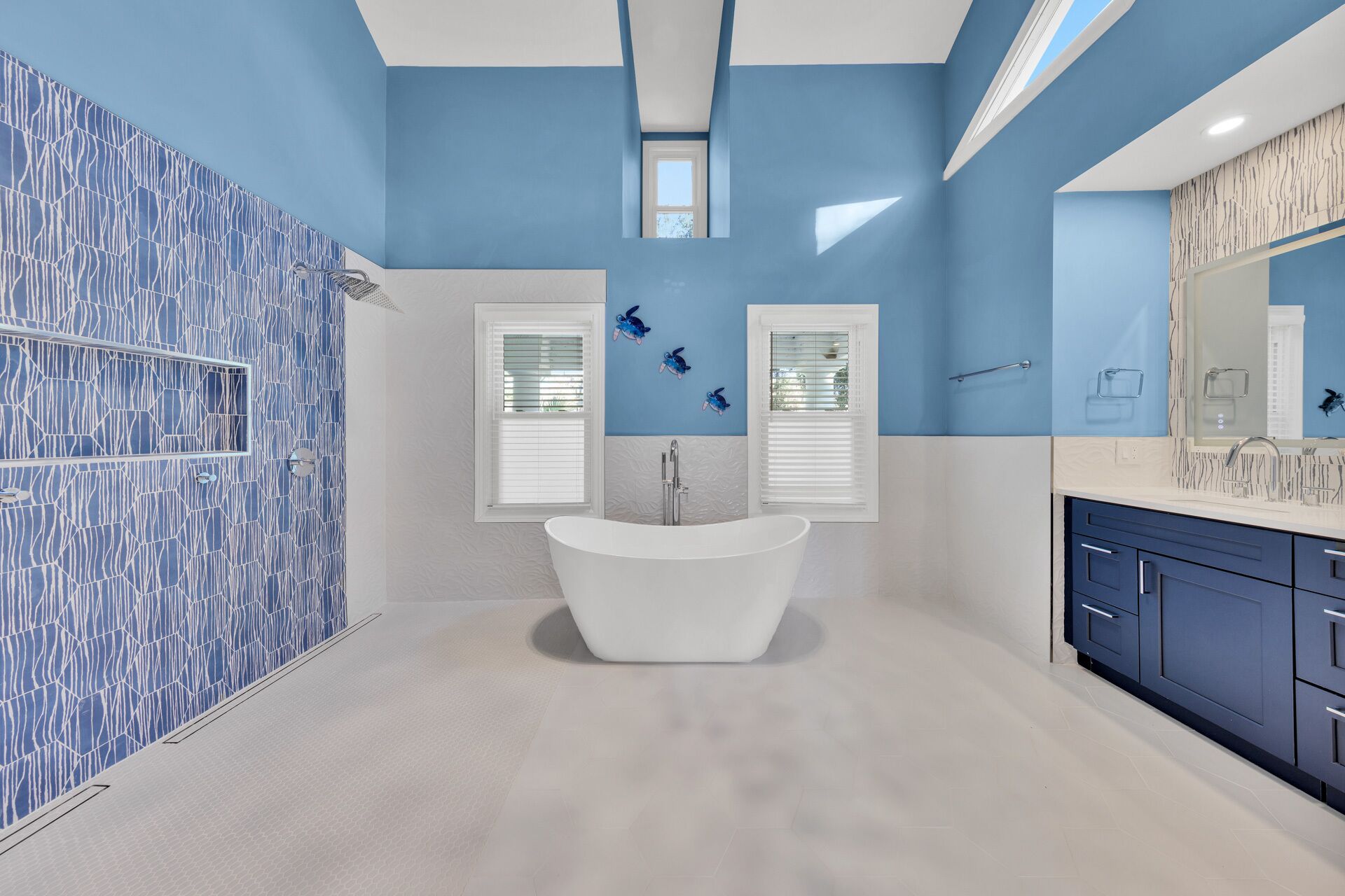 Un baño moderno con una bañera independiente, dos ventanas con persianas y un espejo grande sobre el lavabo.