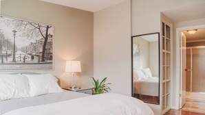 A hotel room with a large bed, a bedside table with a lamp, a potted plant, and a large mirror.