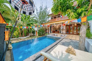 Relax by the serene pool surrounded by lush vegetation and lounge chairs, shaded by a thatched umbrella.