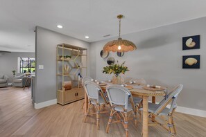 A dining area with a round table, wicker chairs, a hanging light fixture, and a built-in shelving unit. - Welcome to Clipper Casa, your gateway to the ultimate vacation experience! (Naples)