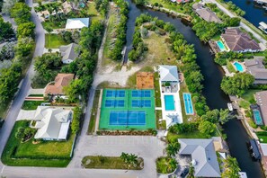 An aerial view of a residential area with a tennis court, swimming pool, and a dock by a river. - Welcome to Clipper Casa, your gateway to the ultimate vacation experience! (Naples)