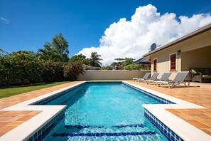 A rectangular swimming pool with blue tiles and a white edge, surrounded by a tiled deck.