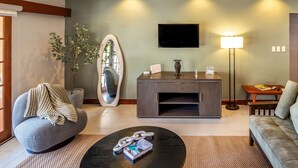 Una sala moderna con un sofá gris, una mesa de centro redonda con revistas, un mueble de madera oscura, una lámpara de pie y un espejo grande.