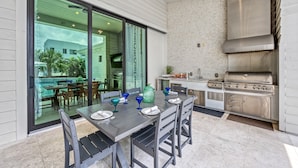 Zona d'esbarjo exterior amb una taula preparada per a quatre persones, una estació de barbacoa i vistes a la piscina i la vegetació.