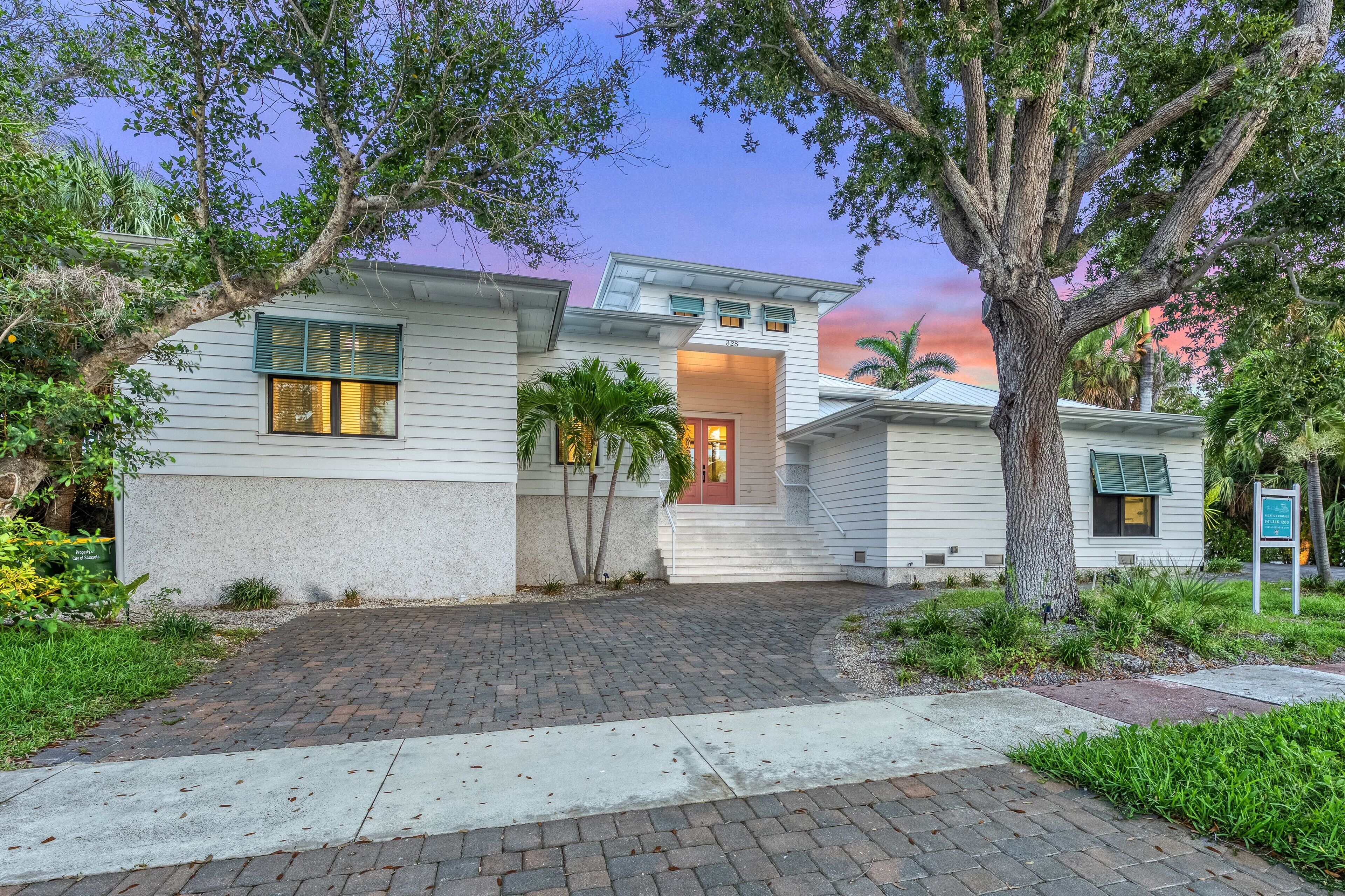A two-story house with a brick driveway, a front porch, and a small garden area.