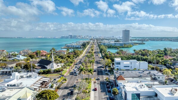 A coastal cityscape with a prominent high-rise building, a marina, and a wide road with vehicles.
