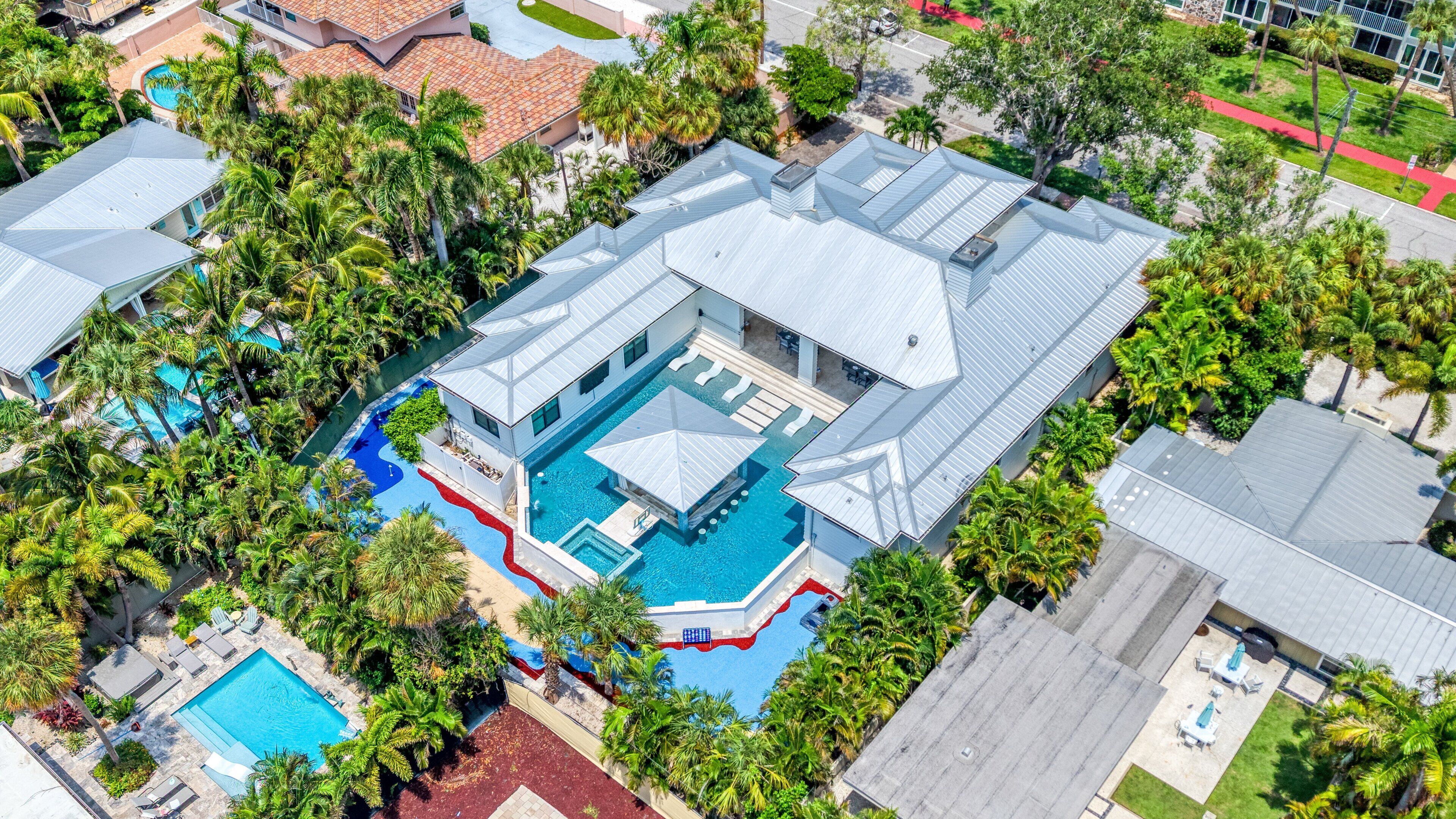A large building with a swimming pool, surrounded by palm trees and other greenery.