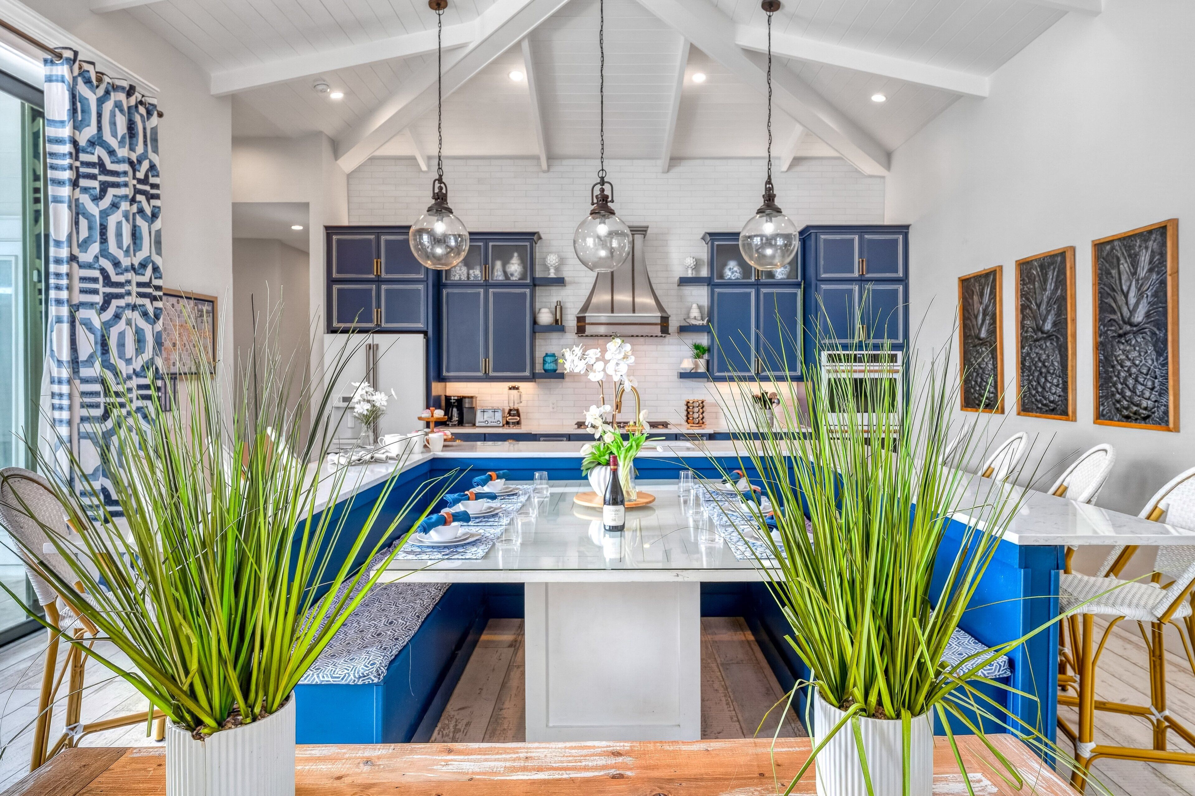 A modern kitchen with blue cabinets, hanging pendant lights, and a central island with a white countertop.