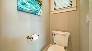 A bathroom with a toilet, a roll of toilet paper, and a window with blinds.