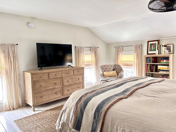 A bedroom with a large bed, a wooden dresser, a television, a chair, and a bookshelf.