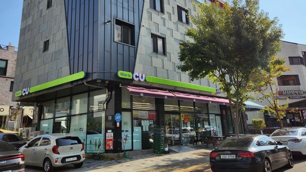 Ein modernes Gebäude mit einem markanten, winkelförmigen Design, ausgestattet mit einer Schaufensterfront und einem grünen Vordach sowie Beschilderung.