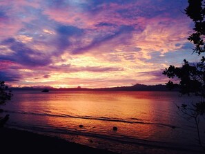 A sunset over a calm body of water with silhouettes of trees and a distant landmass. - Latui Loft, Forest hideaway minutes from Savusavu town (Savusavu)