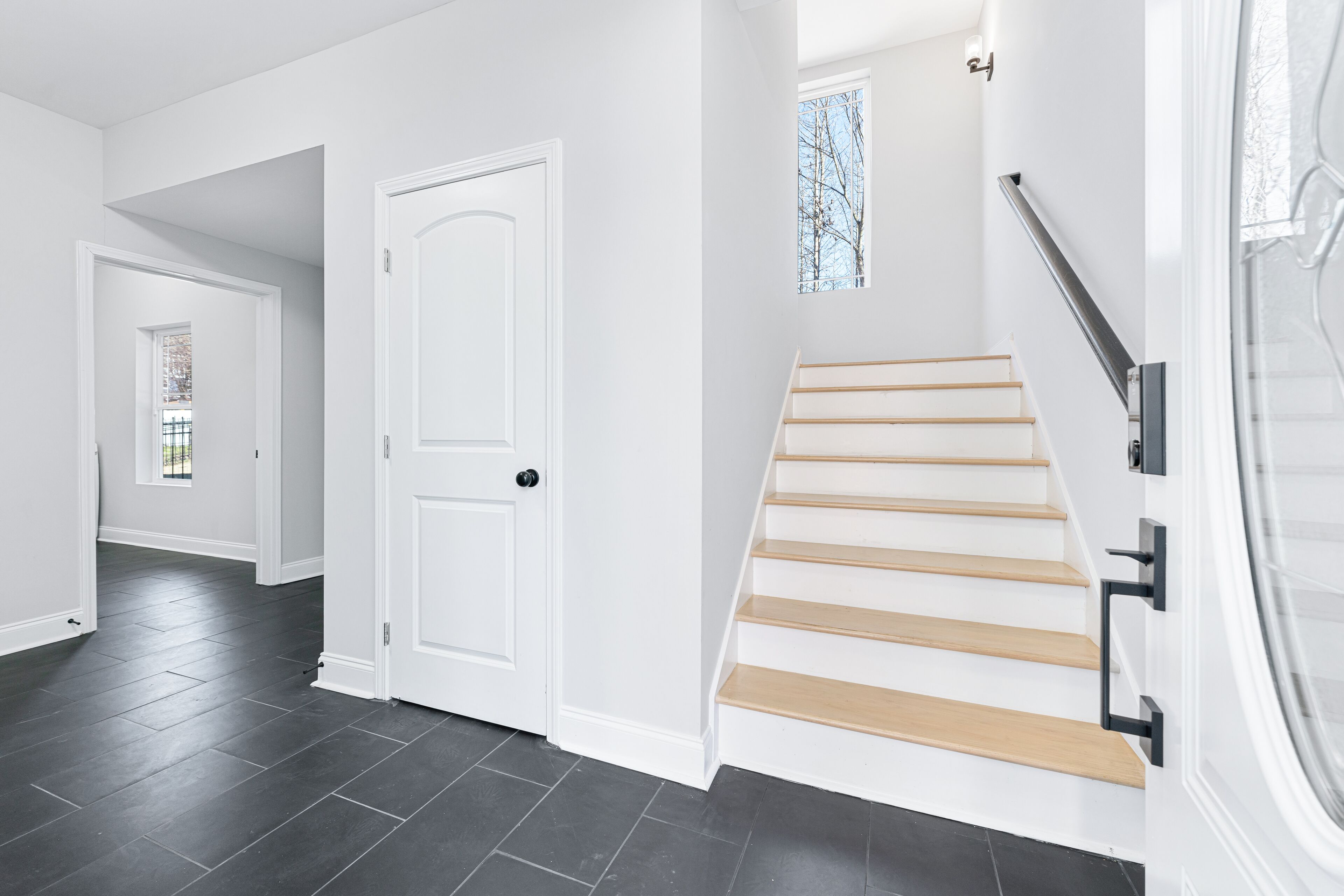 A modern interior with a staircase, a white door, and a view of a garden through a window.