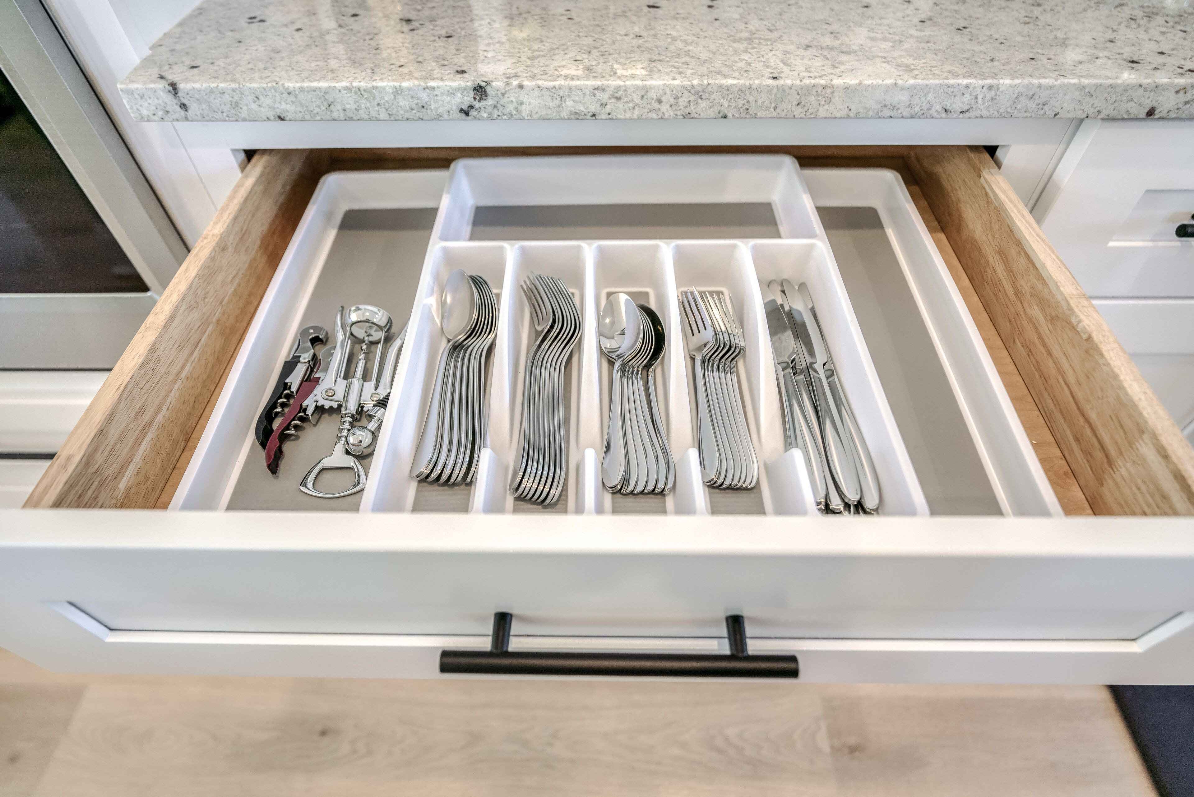 A kitchen drawer with utensils and a bottle opener.
