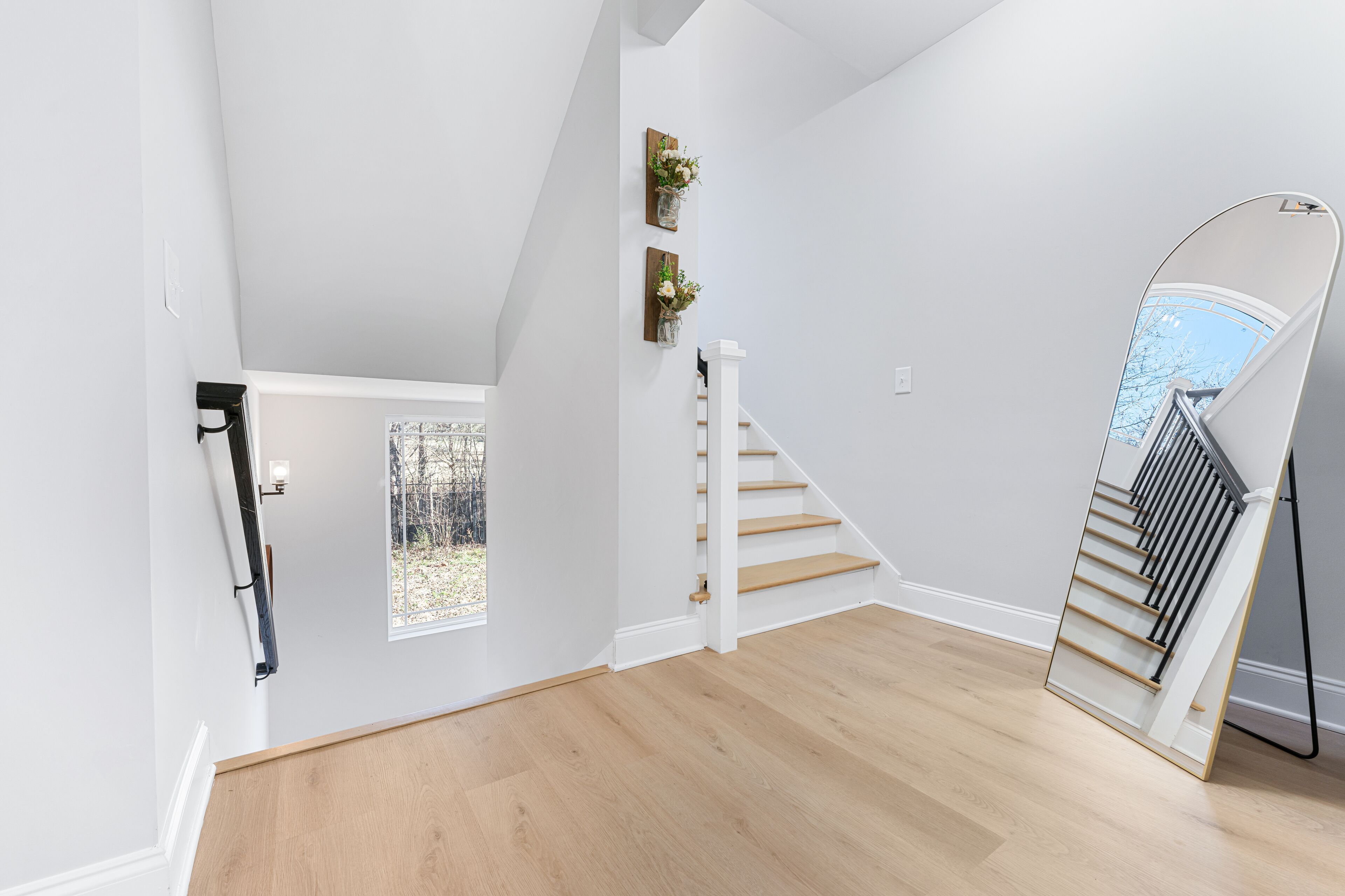 Une pièce spacieuse avec un escalier en bois, des murs blancs et une grande fenêtre.