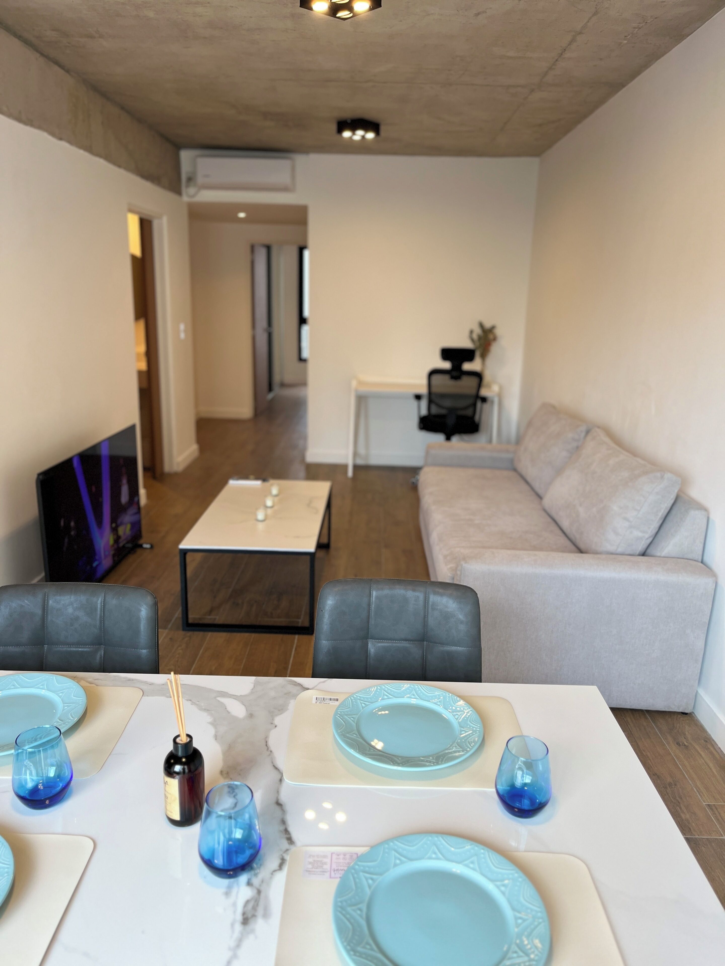 A modern living room with a sofa, a dining table set with plates and glasses, and a TV in the background.
