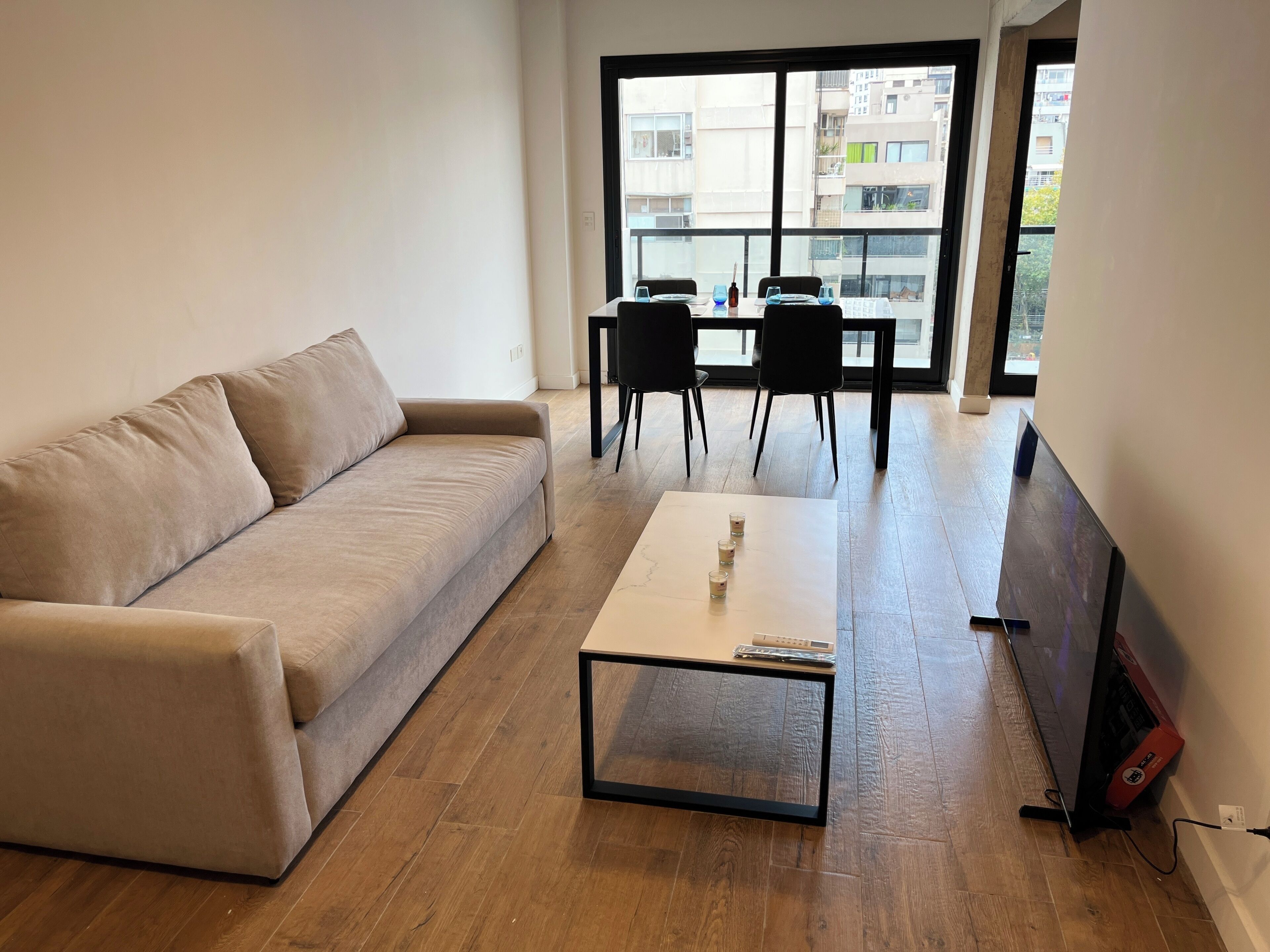 Una sala de estar con un sofá color crema, una mesa de centro, un televisor y un comedor con mesa y sillas.
