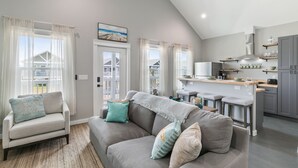 A modern living room with a gray sofa, a coffee table, and a view of the kitchen. - Schipps Creek - Ocean & Bay Views (Bolivar Peninsula)