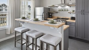 A modern kitchen with a central island, bar stools, a refrigerator, a stove, and built-in shelves. - Schipps Creek - Ocean & Bay Views (Bolivar Peninsula)