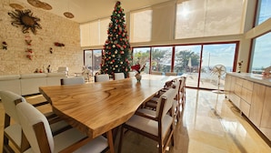 Un espace repas moderne avec une grande table en bois, des chaises blanches et un sapin de Noël décoré.