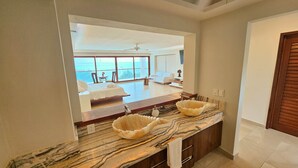 Une salle de bain dotée d’un grand miroir, de deux vasques avec des plans de travail en marbre, et offrant une vue sur une chambre avec balcon.