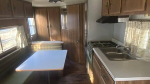 A compact RV kitchen with wooden cabinets, a stove, and a sink.