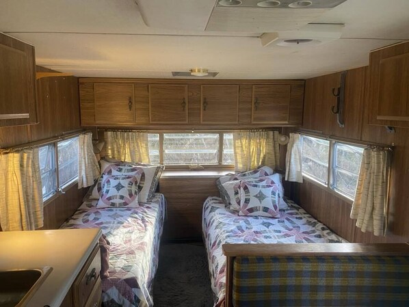 A compact RV interior with two beds, a kitchenette, and a window providing natural light. - COHO CAMPER (Gustavus)