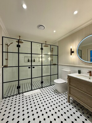 A modern bathroom with a glass-enclosed shower, a toilet, and a vanity with a mirror.