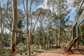 A wooden deck with a lounge chair, surrounded by eucalyptus trees and a modern building with large windows.