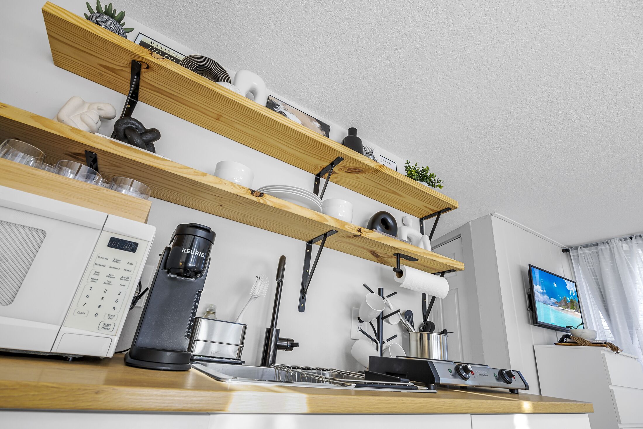 Une cuisine moderne avec des étagères en bois, une machine à café, un four à micro-ondes et un téléviseur.
