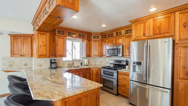 A kitchen with wooden cabinets, stainless steel appliances, granite countertops, and a bar area. - Spacious 6 BR Extended Stay (North Salt Lake)